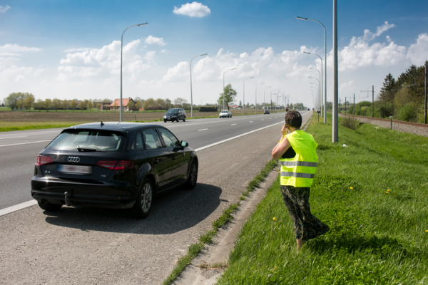 bestuurder in fluohesje met autopech op pechstrook