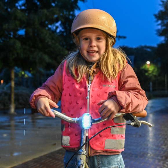 Meisje op fiets in het donker met fluohesje en fietslicht