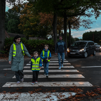 voetgangers in fluohesje oversteken op een zebrapad in het schemerdonker
