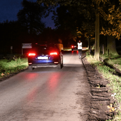 slecht verlichte weg zonder voetpad met jogger in fluohesje, in het donker